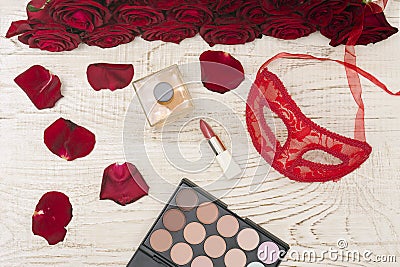 Romantic carnival concept. Red carnival mask, bouquet of red roses, lipstick, bottle of perfume and eye shadow on light wooden Stock Photo