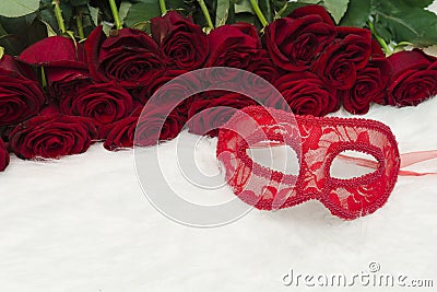 Romantic carnival concept. Red carnival mask and a bouquet of red roses on white fur. Close-up Stock Photo
