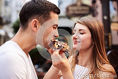 Romantic couple on date eating tasty belgian waffle with chocolate and caramel. Young blond woman, feeding brunette man with yummy Stock Photo