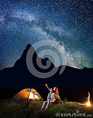Romantic couple hikers looking at the shines starry sky at night. Happy pair sitting near camp and campfire Stock Photo