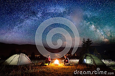 Romantic couple sitting at campfire near tents in the night Stock Photo