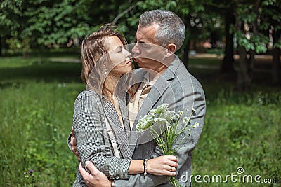 Romantic couple of upset, depressed woman holding bouquet of field flowers, mature man try to kiss female in green park Stock Photo