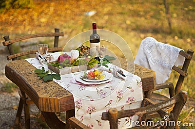 Romantic dinner in the autumn garden, table setting for a nice dinner. Wine, fruit, pomegranate and flowers. Picnic in the open Stock Photo