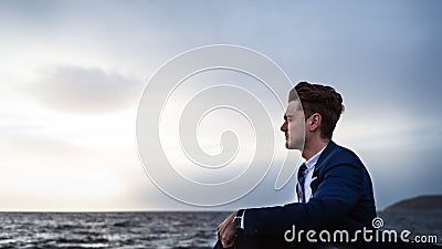 Romantic elegant man in suit sits on the background of the sea and sky Stock Photo
