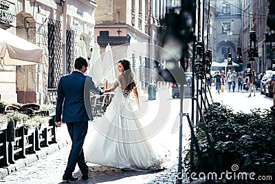 Romantic emotional outdoor portrait of the stylish couple of newlyweds dancing in the sunny street. Stock Photo