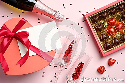 Romantic flat lay composition with champagne bottle, glasses, box of chocolates, heart shaped gift box with blank paper greeting Stock Photo