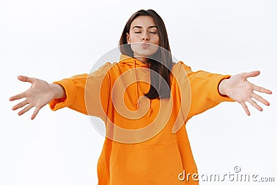 Romantic gorgeous girlfriend in orange hoodie, close eyes and fold lips for mwah, reaching hands forward to cuddle and Stock Photo