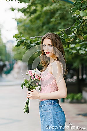 Romantic image of a young girl walking on a summer street in the Park with a bouquet of roses Stock Photo
