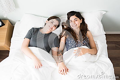 Top view of happy LGBT girlfriends in bed smiling at the camera Stock Photo