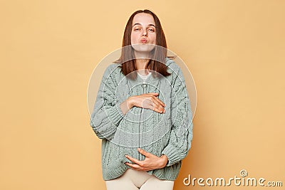 Romantic loving pregnant woman future mother wearing knitted warm sweater standing isolated over beige background sending air Stock Photo