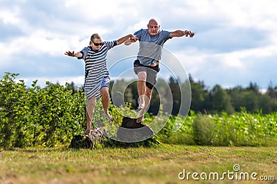 Romantic middle-aged couple holding hands jumping from a stone, the concept of a happy relationship Stock Photo