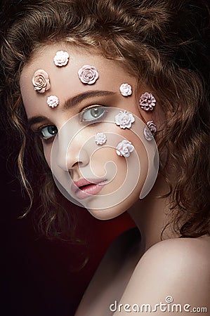 Romantic nude young beautiful girl with white flowers on her face and soft curls on dark background. Stock Photo