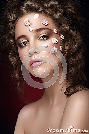 Romantic nude young beautiful girl with white flowers on her face and soft curls on dark background. Stock Photo