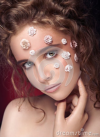 Romantic nude young beautiful girl with white flowers on her face and soft curls on dark background. Stock Photo