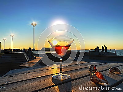 Romantic people silhouette at sunset down light glass of orange cocktail on wooden table and seashell blue sky seaside panora Stock Photo