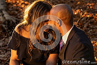Romantic photo of a well dressed mixed race couple hugging and holding kissing each other at sunset in a city park Stock Photo