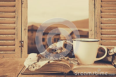 Romantic scene of cup of coffee next to old book in front of countryside view outside of the old rustic window Stock Photo
