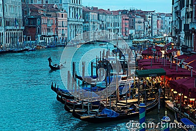 Romantic scenery of tourists riding in a gondola on Grand Canal at sunset, with ferry boats parking by restaurants & bars Editorial Stock Photo