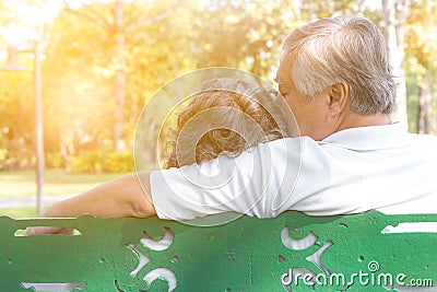 Romantic senior couple. Grandfather embracing, kissing grandmother. Lovely elderly couple sitting on bench at park. Elderly man an Stock Photo