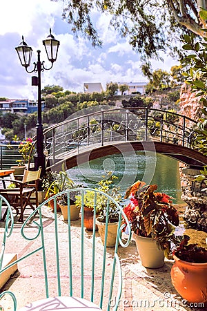 Romantic style coffee shop. Charming garden of cafe with stylish decor. Bridge over the lake, metalwork chair, lantern and plants. Stock Photo