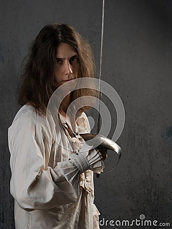 Romantic young man in a medieval costume with a sword in his hands, a musketeer in a fighting stance, Stock Photo