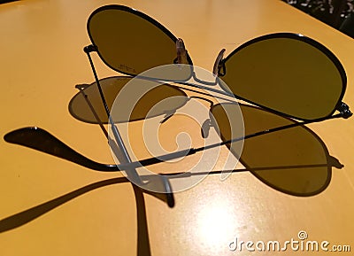 Ray-Ban polarized glasses cast shadow on yellow formica table. brand of sunglasses and eyeglasses designed for aviators by Bausch Editorial Stock Photo