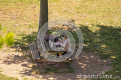 Girl in a mask and gloves during self-isolation reading news on cell phone at a table under the tree in the park in Rome Editorial Stock Photo