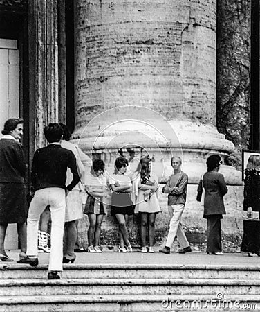 Rome, Italy, 1970 - Three girls in miniskirts rest in the crowd at the foot of a column Editorial Stock Photo