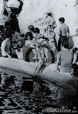 ROME, ITALY, 1970 - A young, blonde female tourist reads a book quietly while refreshing her feet in the Trevi fountain Editorial Stock Photo