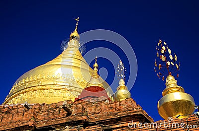 Roof of ancient brick stone temple with golden dome contrasting with deep blue sky - Bagan, Myanmar Stock Photo