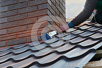 Roofer builder worker attach metal sheet to the chimney. Unfinished roof construction Stock Photo