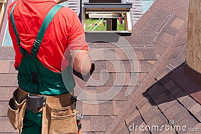 Roofer builder worker with bag of tools installing roofing shingles. Stock Photo