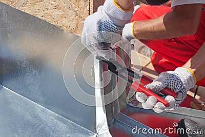 Roofer builder worker finishing folding a metal sheet using special pliers with a large flat grip. Stock Photo