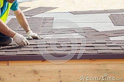 Roofer builder worker installing Asphalt Shingles or Bitumen Tiles on a new house under construction Stock Photo