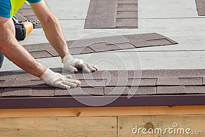 Roofer builder worker installing Asphalt Shingles or Bitumen Tiles on a new house under construction Stock Photo