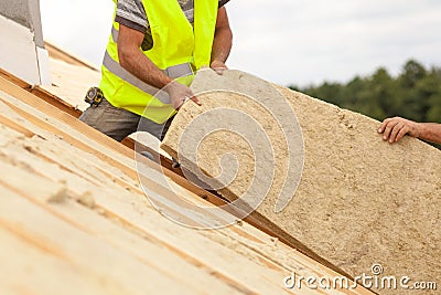 Roofer builder worker installing roof insulation material on new house under construction. Stock Photo