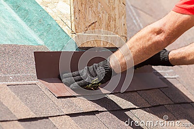 Roofer builder worker installing shingles on a new wooden roof with skylight. Stock Photo