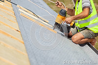 Roofer builder worker use automatic nailgun to attach roofing membrane. Stock Photo