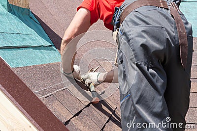 Roofer builder worker use a hammer for installing roofing shingles. Stock Photo