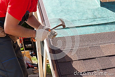 Roofer builder worker use a hammer for installing roofing shingles. Stock Photo