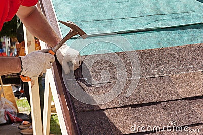 Roofer builder worker use a hammer for installing roofing shingles. Stock Photo