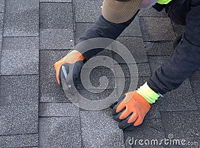 Roofer cuts a shingle to fit during repair work. Stock Photo