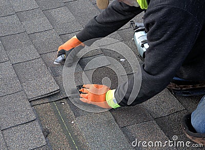 Roofer cuts a shingle to fit during repair work. Stock Photo