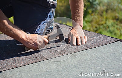 Roofer installing asphalt shingles on house construction roof corner with hammer and nails. Roofing construction. Stock Photo