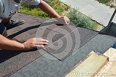 Roofer installing asphalt shingles on house construction roof corner. Roofing construction. Stock Photo