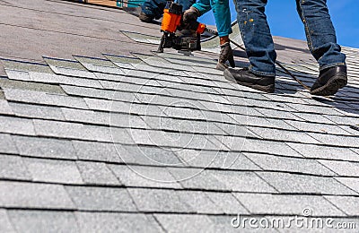 Roofer installing roof shingles with nail gun Stock Photo