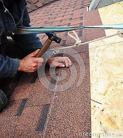 Roofer installs bitumen roof shingles with hammer and nails. Roofing Stock Photo