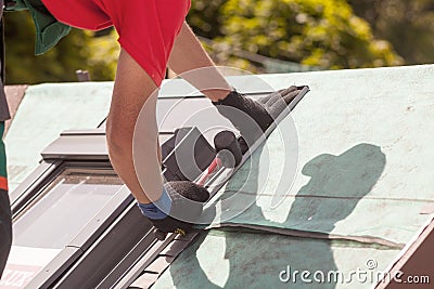 Roofer installs metal profile on a roof window with a rubber mallet. Stock Photo