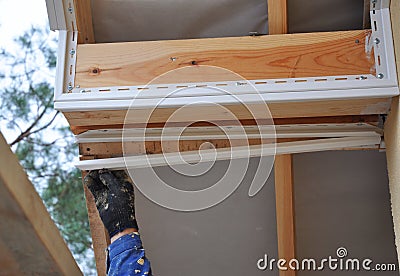 Roofer worker uses a hand to install soffit, eaves, wooden beams. Stock Photo