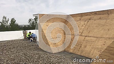 Roofers repairing areas of a commercial flat roof, wood panel base of a built up wall Editorial Stock Photo